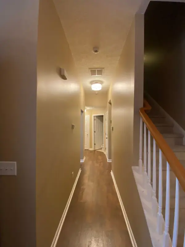 Long hallway with warm tan walls beside a white-spindled stair, Bellevue, TN