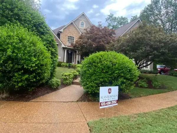Brick house front behind shrubs with a yard sign, Franklin, TN