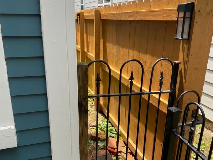 Stained privacy fence along a narrow side yard behind a black iron gate, the kind of detail that shapes a Fairview fence staining estimate