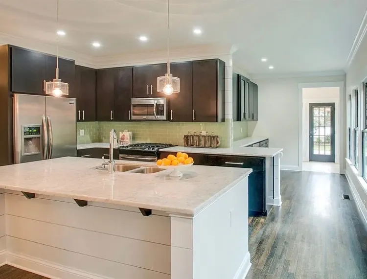 Kitchen with a white-painted island under pendant lights beside warm wood cabinetry, part of the cabinet painting we do for Bellevue homes