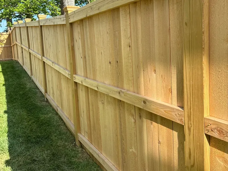 Long privacy fence in a light natural stain, posts and rails along a side lawn, fence staining for a Fairview home