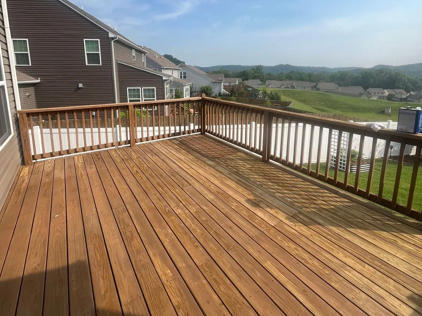 Long stained deck with a wood railing overlooking rolling hills behind a sided house, part of the deck staining we do for Franklin homes