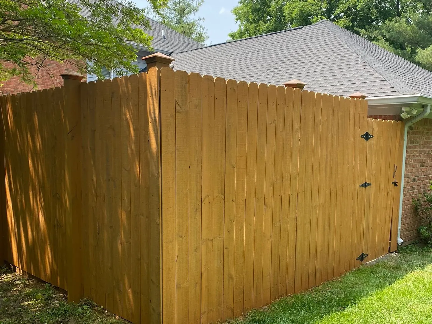 Stained privacy fence corner with a black-hinged gate beside a brick house, fence staining for a Nashville home
