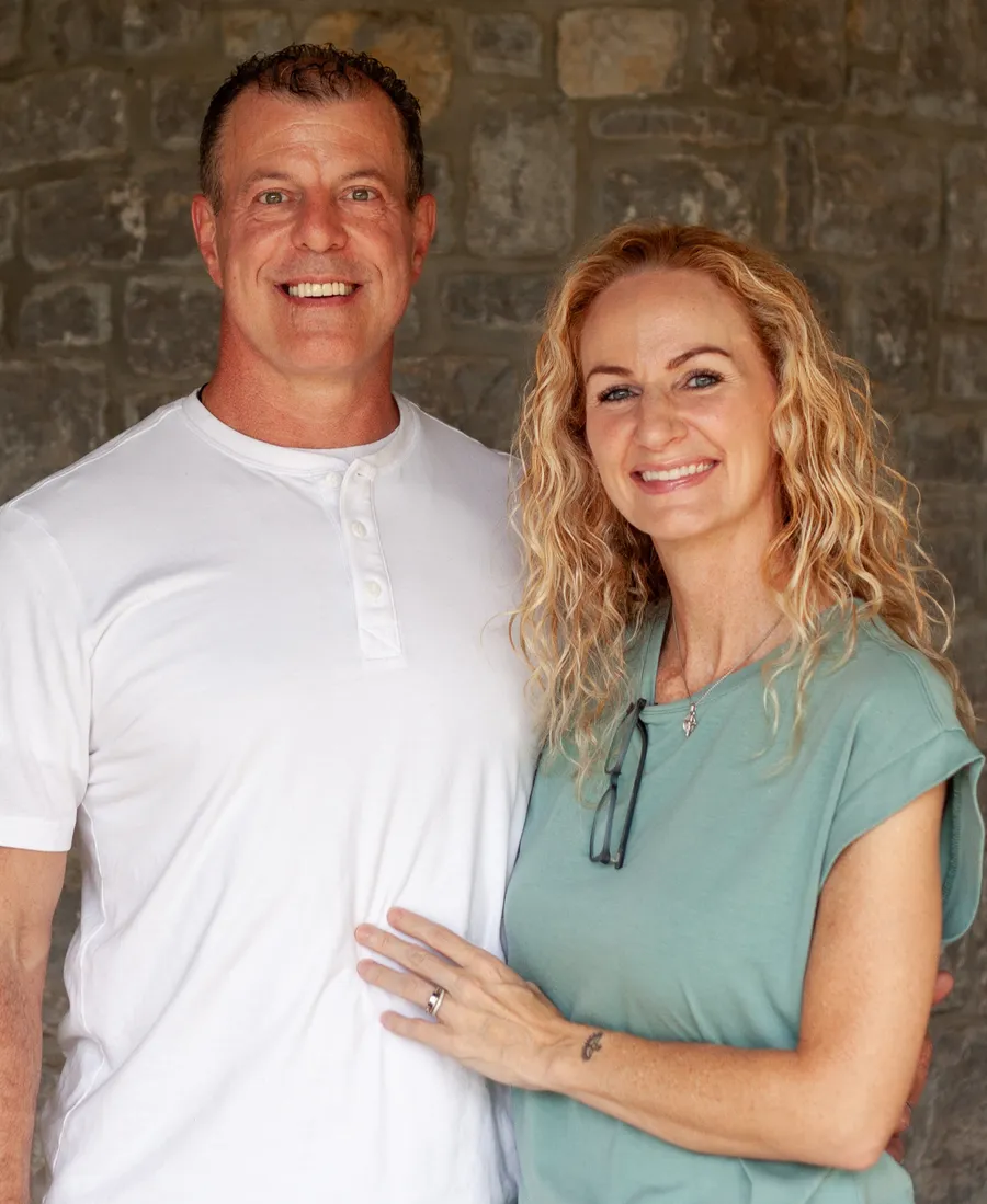 Beth Robinson smiling beside her husband Alan in front of a stone wall, part of the Robinson family business serving Bellevue