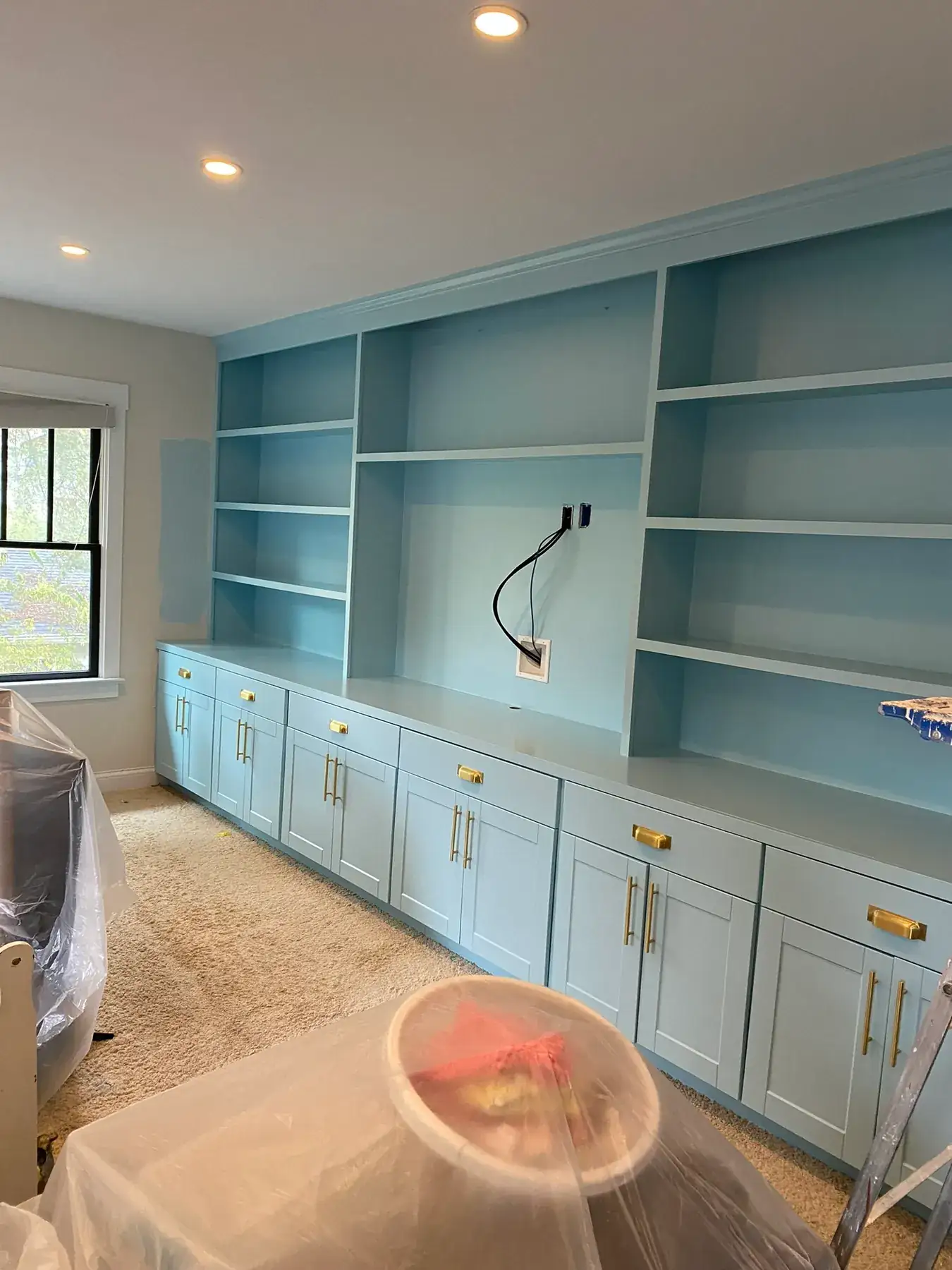 Built-in shelving and cabinets painted soft blue, the room still under protective plastic, one of our cabinet painting projects for Bellevue homes