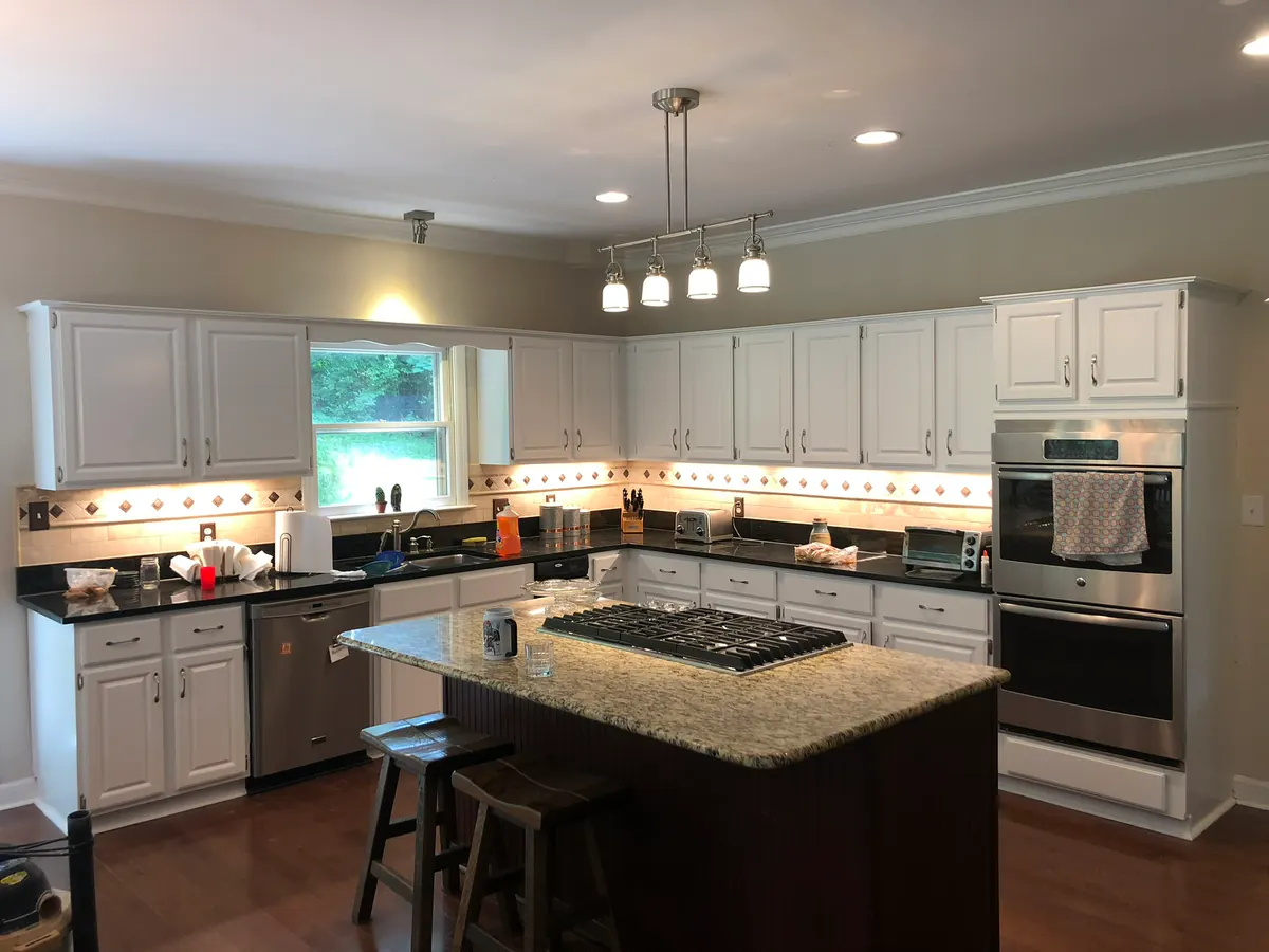 Kitchen cabinets and a large island painted clean white around wall ovens and a cooktop, cabinet painting for a Bellevue home