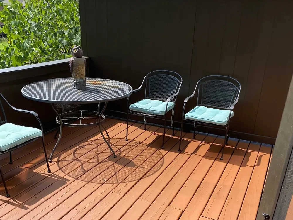 Deck stained a rich brown with a patio table beside a dark privacy wall, deck staining for a Fairview home