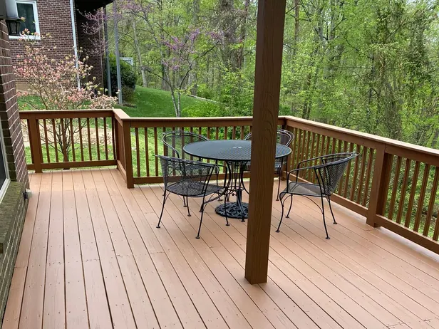 Long stained deck with a wood railing and a patio table beyond a support post, deck staining for a Fairview home