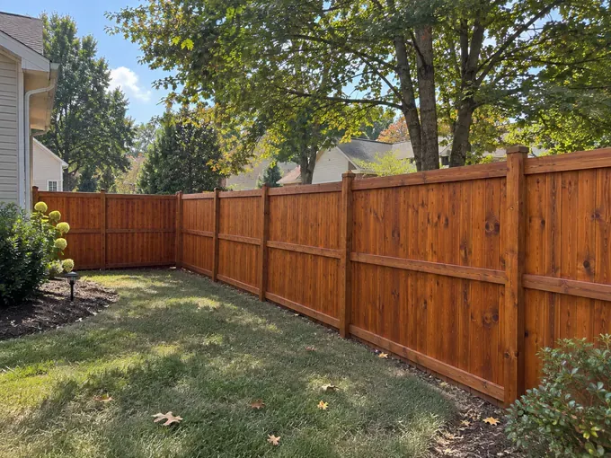 Corner of a stained cedar privacy fence beside the house in a small backyard, fence staining for a Belle Meade home