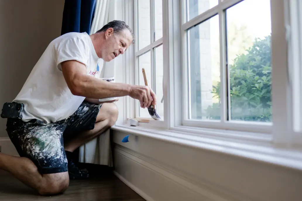 Painter cutting in along a bank of windows by hand, interior painting for a Fairview home