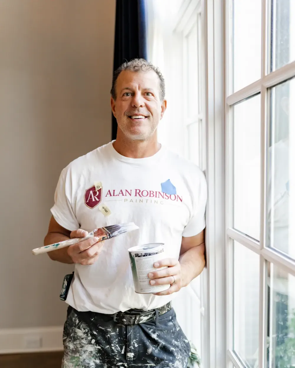 Alan Robinson with a brush and a paint bucket at a window