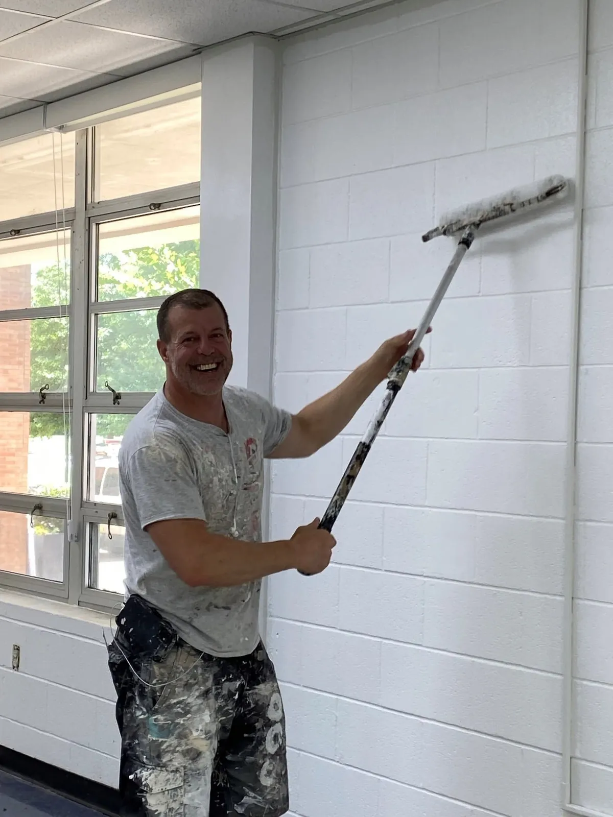 Alan Robinson rolling white paint onto a block wall in the Overbrook Catholic School science lab