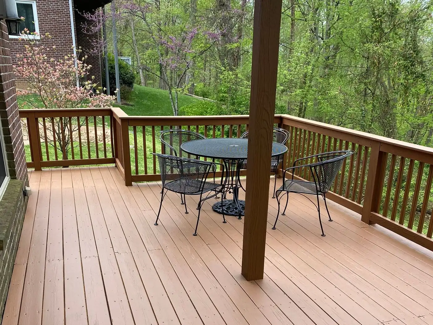 Long stained deck with a wood railing and a patio table beyond a support post, deck staining for Nashville homes