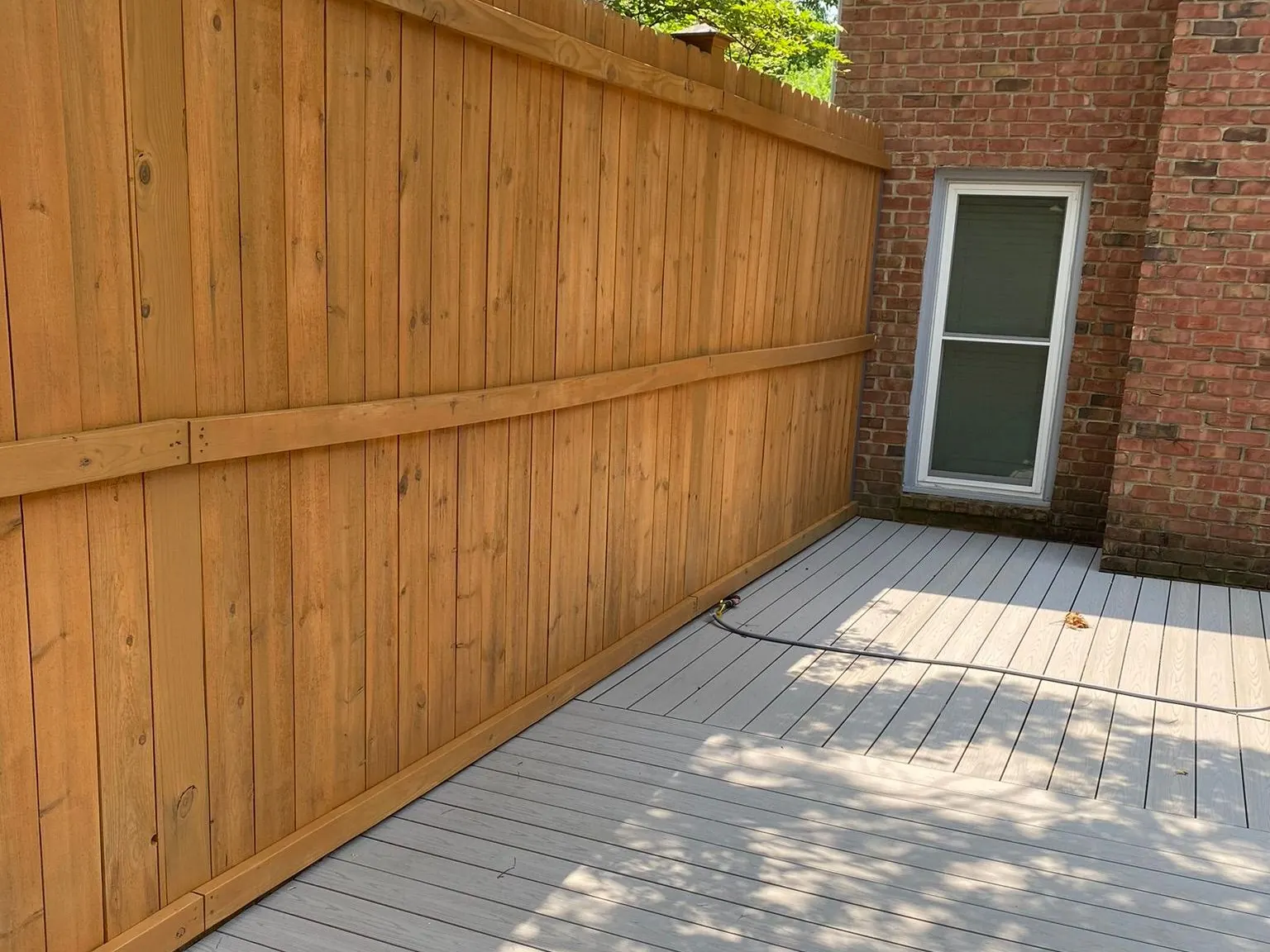 Cedar-stained privacy fence running along a gray deck beside a brick house, fence staining for Nashville homes