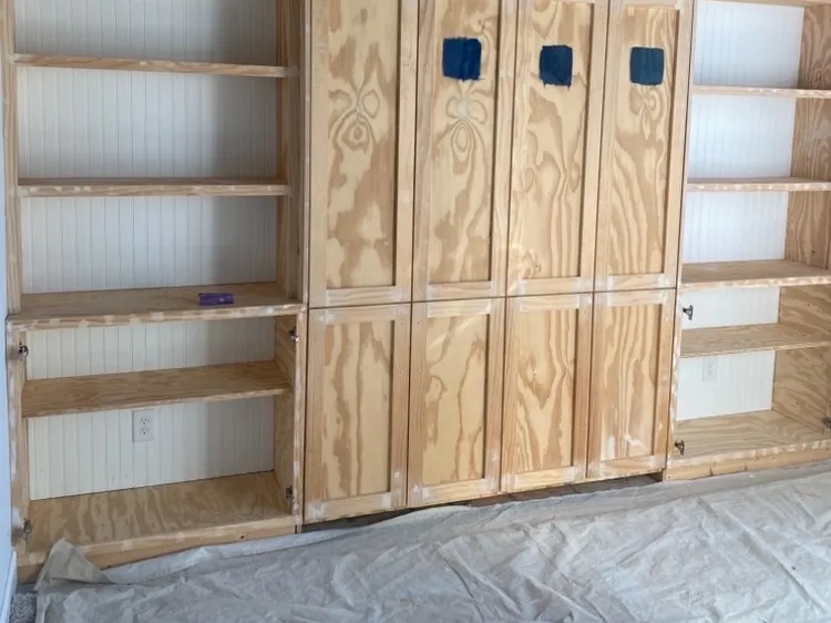 Bare wood built-ins mid-prep, nail holes filled and a canvas drop cloth over the floor, a step in our cabinet painting process for Bellevue homes
