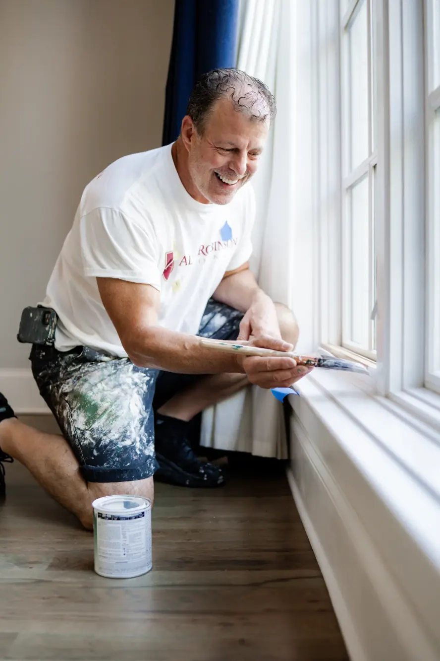 Alan Robinson kneeling at a window, cutting in the sill and casing with an angled brush, a step in our interior painting process for Bellevue homes